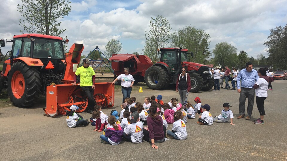 Des enfants sont assis devant un tracteur et écoutent la formation pour en comprendre les dangers.