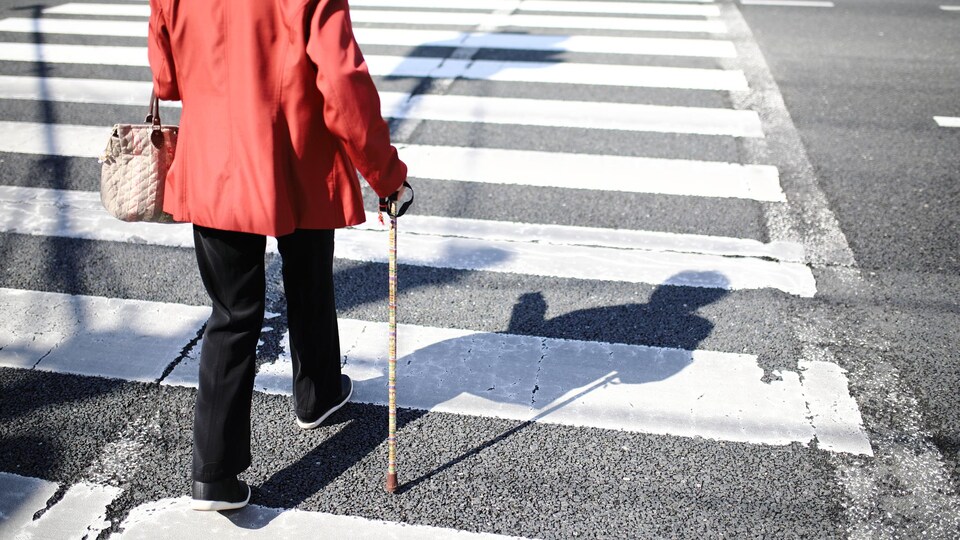Une femme d'un certain âge traverse la rue à l'aide d'une canne.