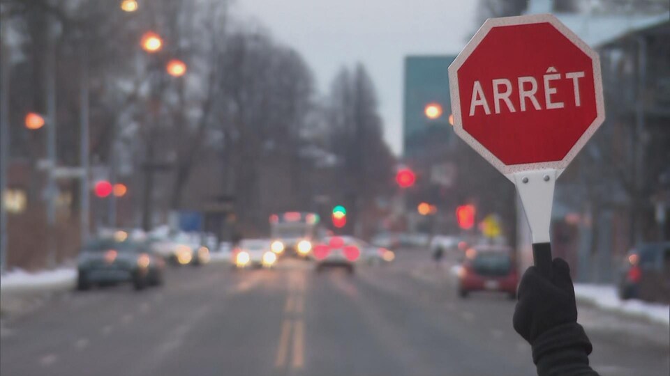 Une main gantée brandissant un panneau «Arrêt dans une rue», en hiver.