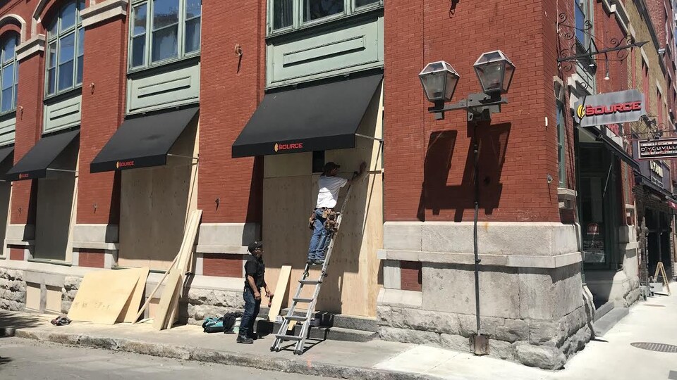 Des ouvriers couvrent les fenêtres d’une boutique La Source à l’aide de panneaux de bois. 