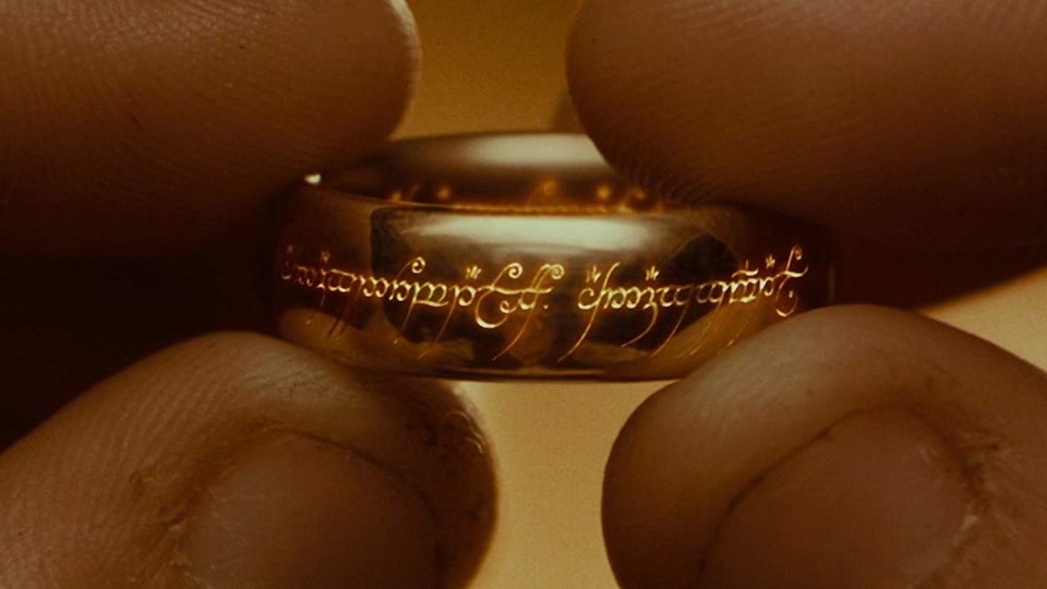 Deux mains tiennent un anneau doré entre leurs doigts. 