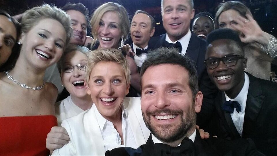 Ellen DeGeneres entourée d'une dizaine de vedettes souriant à la caméra.