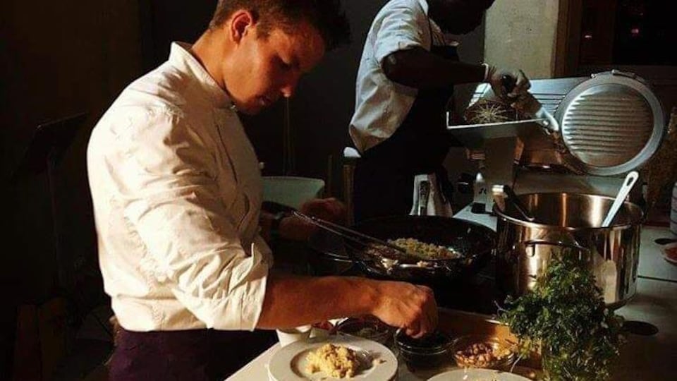 un homme en tenue de cuisine qui termine la préparation d'un plat.