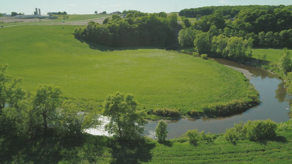 Une terre agricole avec une ferme au loin, et la rivière qui serpente en avant plan.