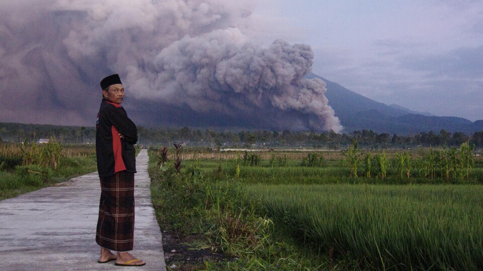 Un Indonésien en premier plan et le volcan en fumée en arrière.