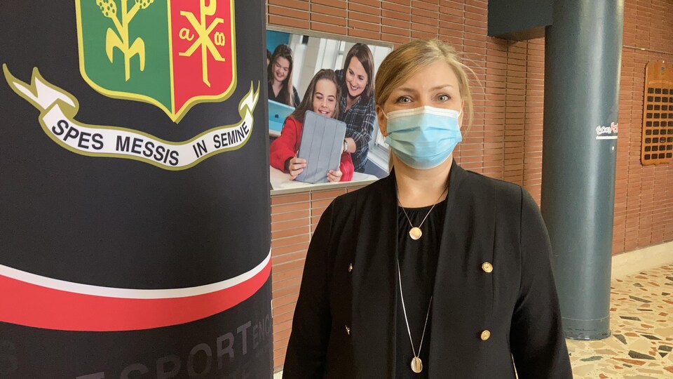 A masked woman poses at a school near a poster.