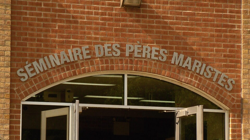 Entrée principale du Séminaire des Pères Maristes. On aperçoit le nom de l’établissement inscrit en lettres grises au-dessus d’une double porte vitrée. La façade de l’édifice est en brique.
