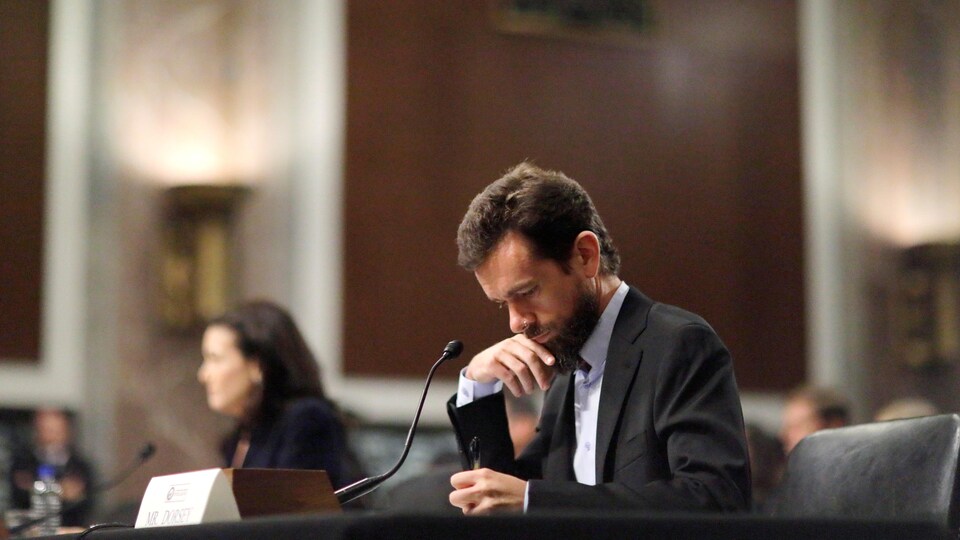 Mme Sandberg est hors-champ. M. Dorsey a l'air pensif alors qu'il prend des notes. Les deux sont assis à la table des témoins.