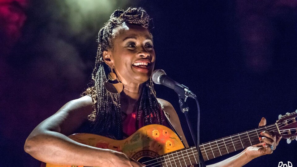 La femme chante et joue de la guitare sur scène. 