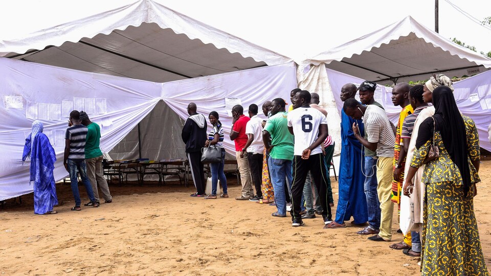 Des Sénégalais font la file en-dehors d'une tente blanche pour le vote.