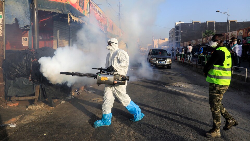 Un homme portant un masque et une combinaison désinfecte une rue.