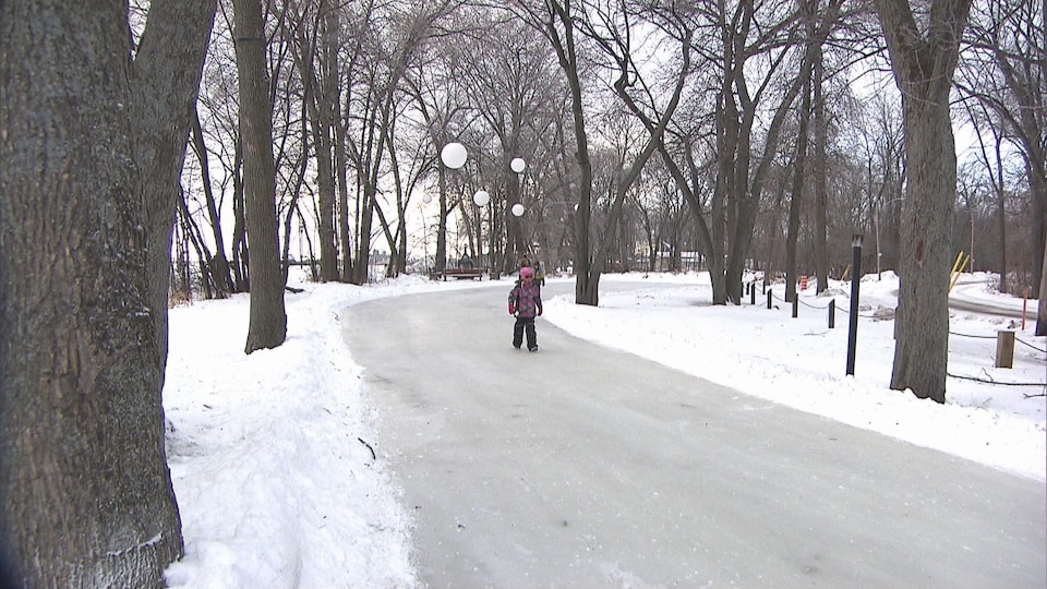 Une fillette marche sur un sentier glacé entouré d'arbres en hiver.