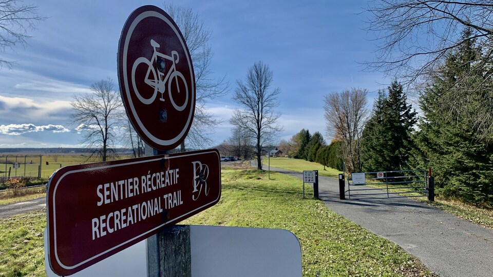 Un panneau indiquant sentier récréatif devant une route et une barrière.