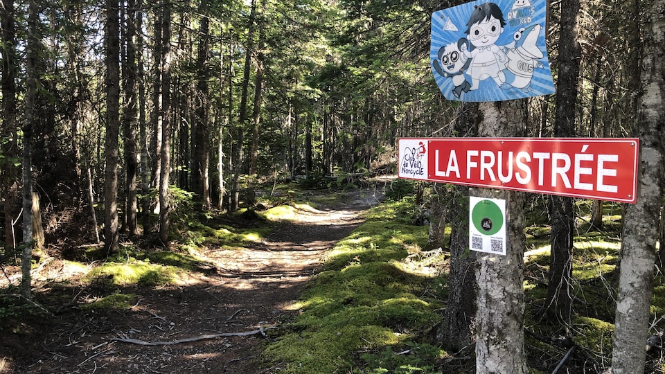 Un sentier de vélo dans le bois. Une pancarte avec le nom de la piste « La frustrée ». 