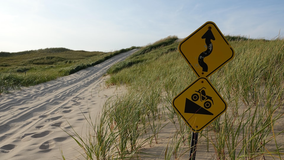 Un sentier de VTT dans le sable des dunes avec un panneau de signalisation qui indique une côte.