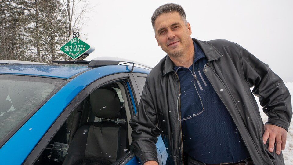 un chauffeur de taxi appuyé sur sa voiture.