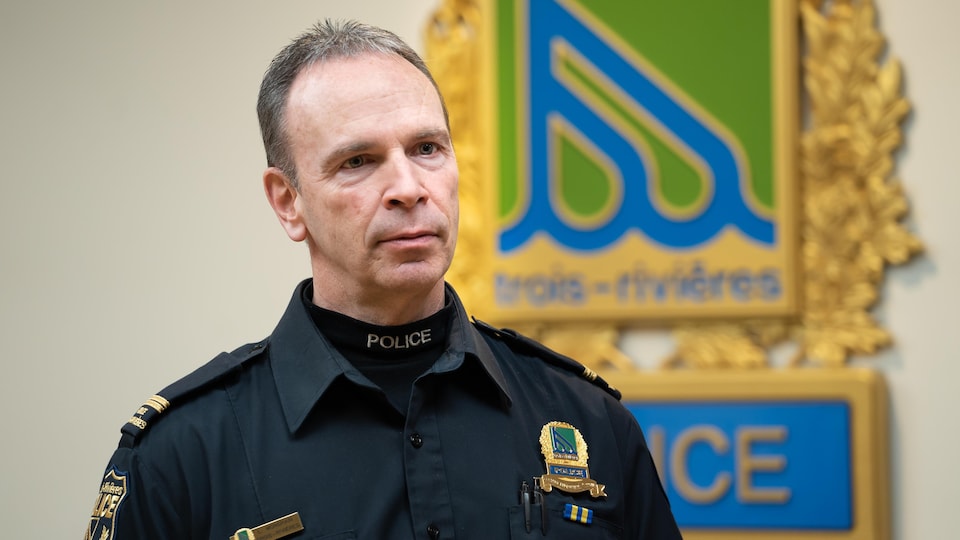 Luc Mongrain in an office, in front of the Trois-Rivières police logo.