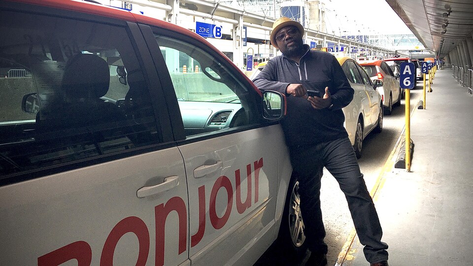 Sergo Charles, appuyé sur le capot de son taxi, dans la zone des arrivées à l'aéroport.