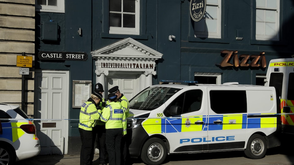 Quatre policiers discutent devant une camionnette de la police britannique stationnée devant le restaurant Zizzi. 