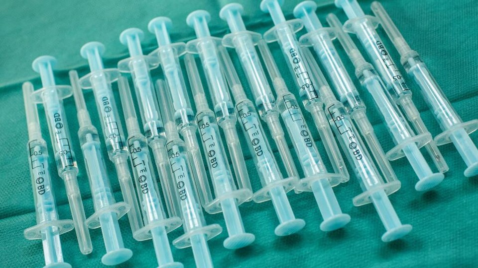 Près d'une vingtaine de seringues contenant une dose d'AstraZeneca sur une surface recouverte de tissu.