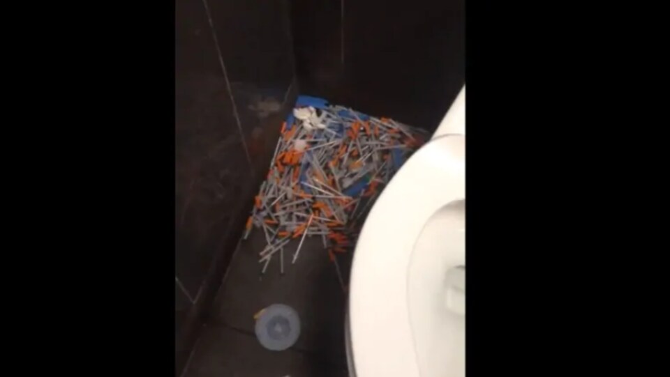 Un amas de seringues à côté d'un siège de toilette.