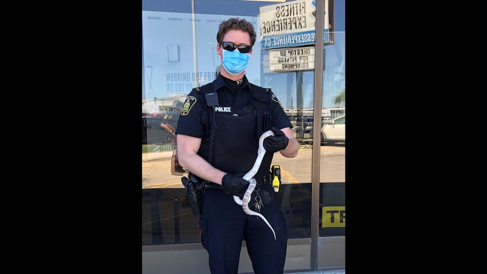 Un policier en masque et en lunettes de soleil tient un petit serpent. 