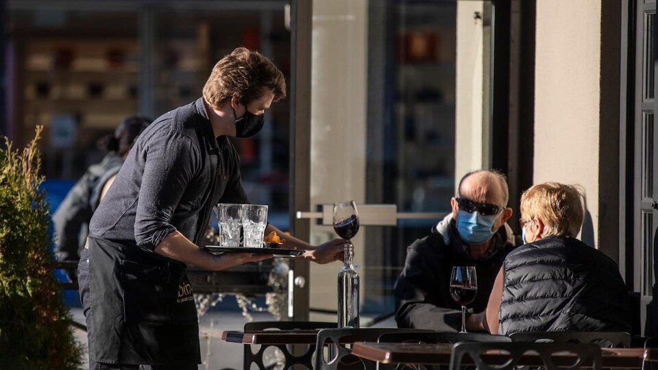Un serveur dépose des verres de vin à une table sur la terrasse d'un restaurant à Vancouver.
