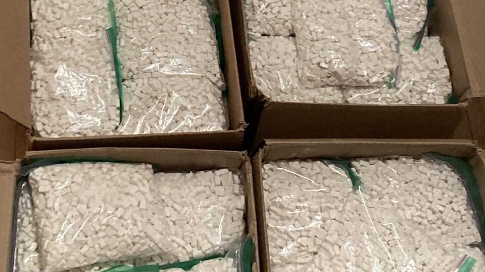 Des milliers de comprimés de méthamphétamines sont emballés dans des sachets de plastique qui se trouvent dans des boîtes en carton.