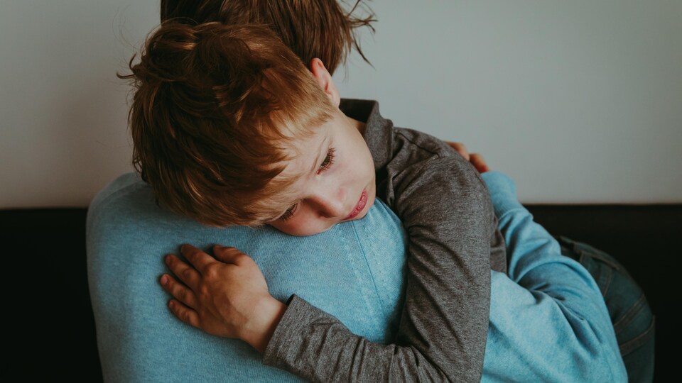 Une personne porte dans ses bras un enfant triste.