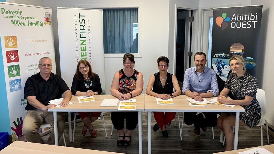 Six personnes assises à une table sourient.