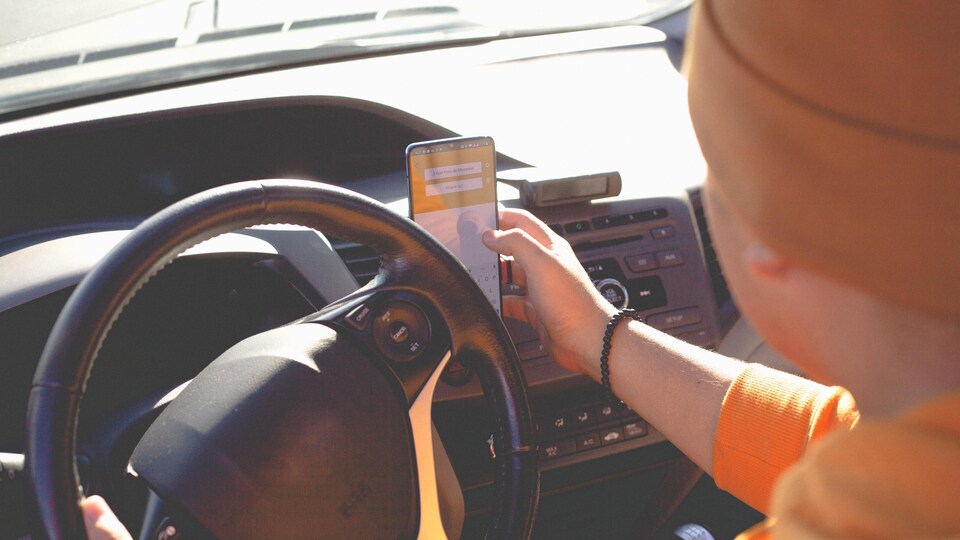 Un livreur entre quelque chose sur son cellulaire au volant de sa voiture.