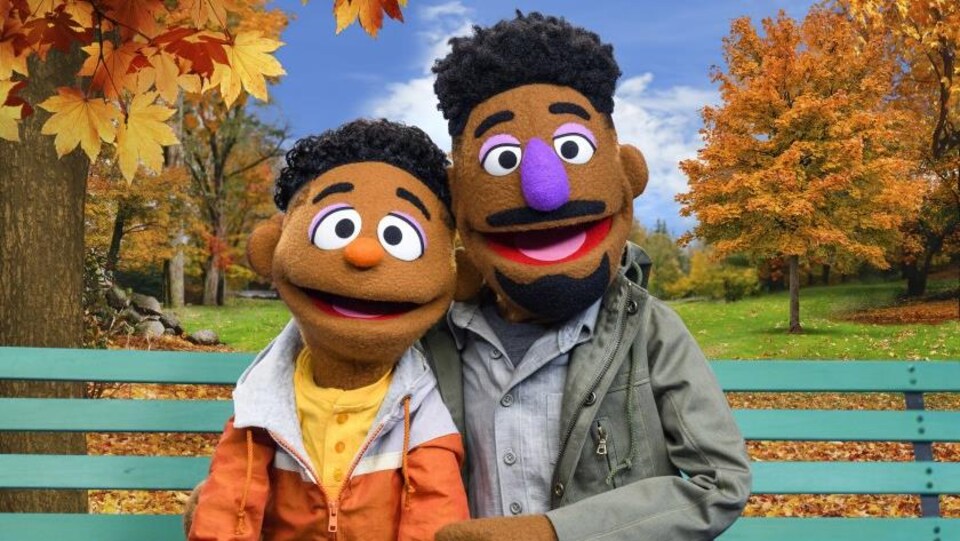 Deux marionnettes représentant un père et un fils afroaméricains sont assises sur un banc dans un parc.