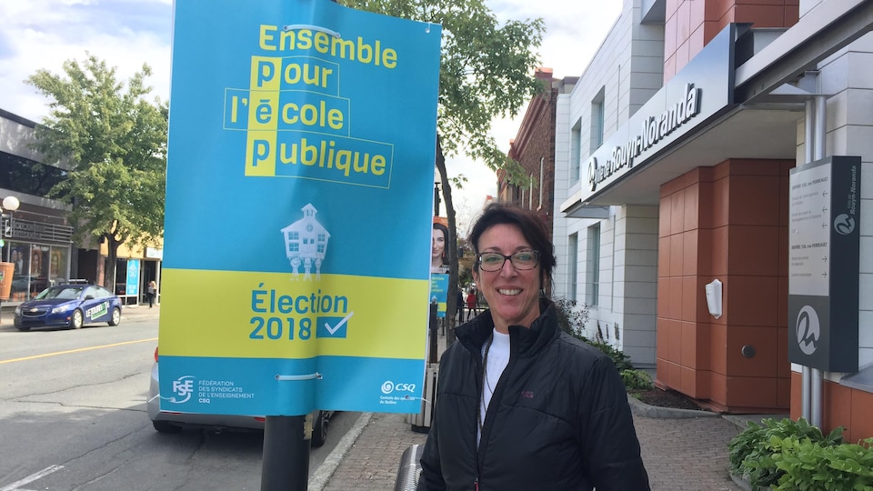 Une femme pose à côté d'une affiche «Ensemble pour l'école publique» dans le cadre de la campagne électorale.