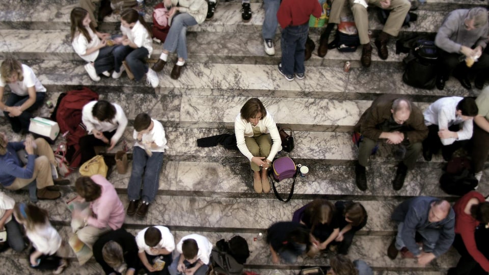 Une femme est assise sur les marches d'un escalier. Elle est entourée d'une foule.