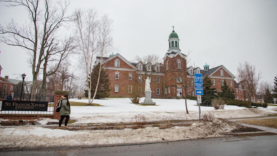 Une femme marche devant l'édifice principal de l'université en hiver.