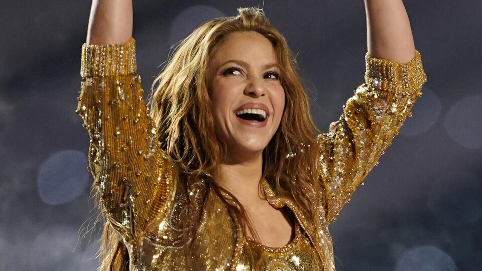 Shakira sorri e joga os braços no ar. 