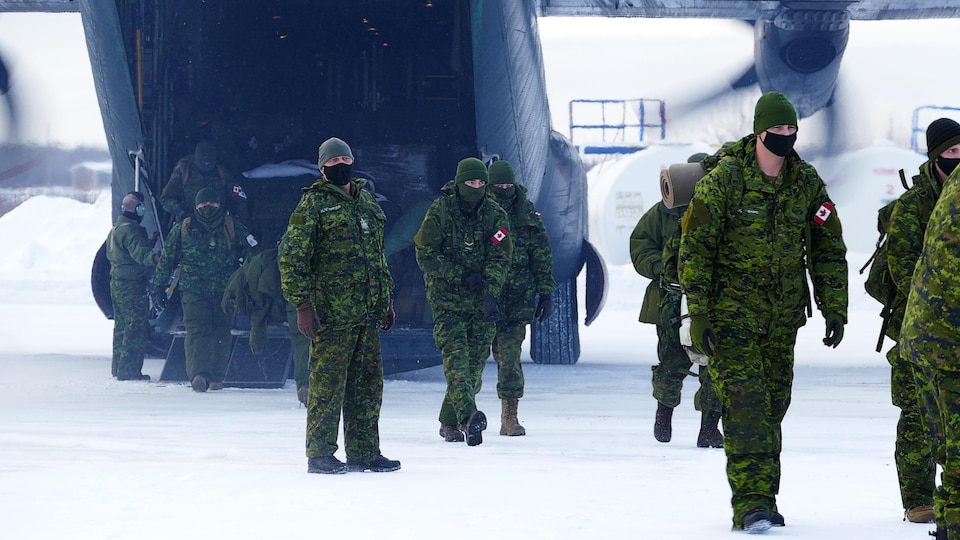 Des militaires débarquent d'un avion dans un environnement hivernal.