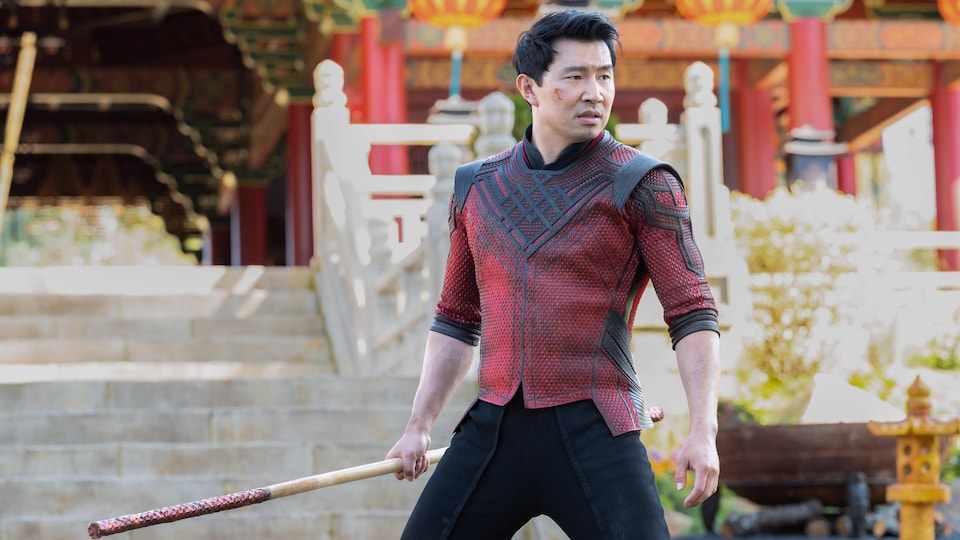 Un homme tient un bâton de combat devant un temple. 