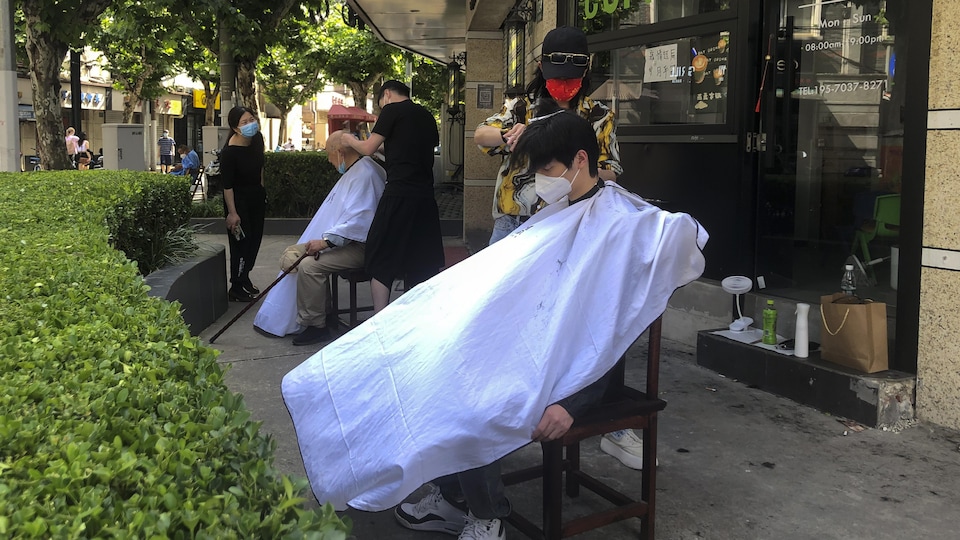 Barbers wearing face masks cut customers ’hair outside a cafe.