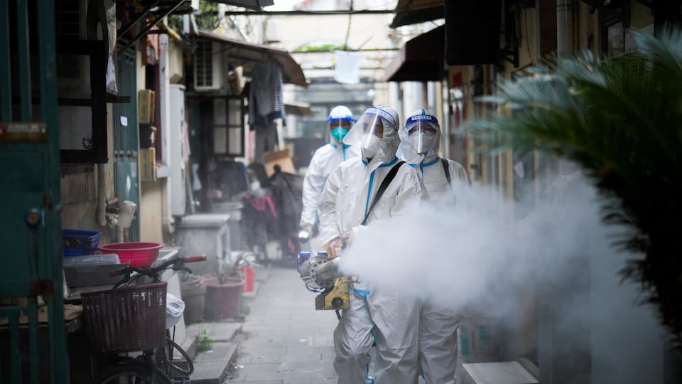 Des travailleurs vêtus d'habits de protection désinfectent un quartier de Shanghai.