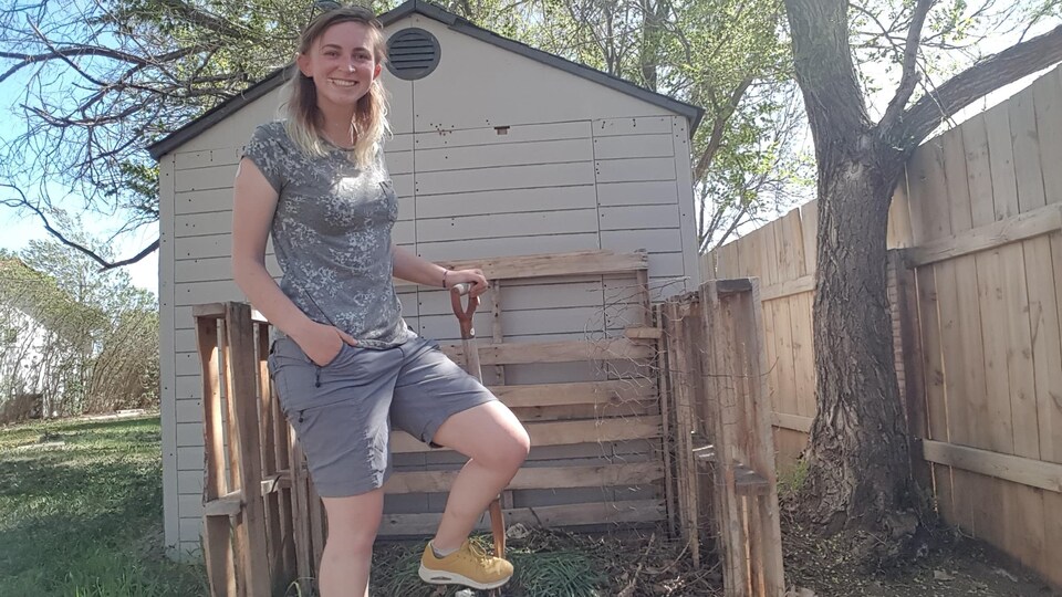 Shannie Boudreault se tient debout devant une pile de compostage avec une pelle à la main.