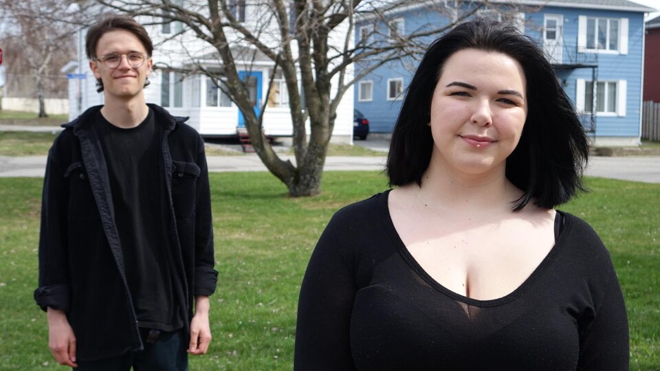 Un jeune homme et une jeune femme regardent la caméra, debouts, à l'extérieur.