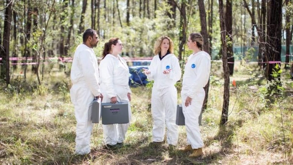 Quatre personnes en combinaison blanche discutent dans un boisé.