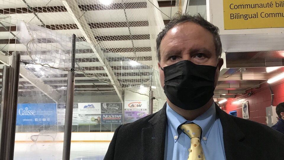 Shaun Chornley est debout devant un aréna de hockey. Il porte une chemise, une cravate et un masque. 