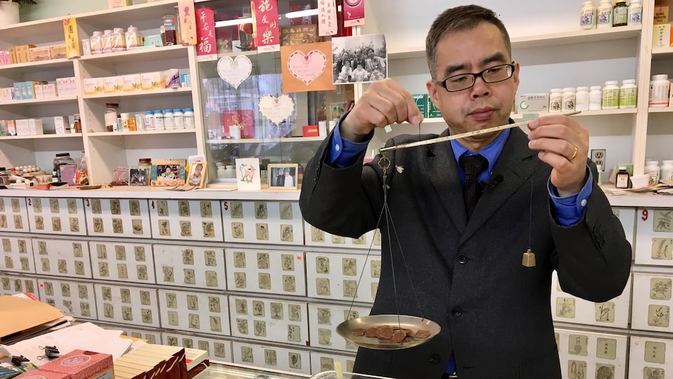 Shawn Yang, dans sa boutique d'Edmonton, utilise une balance « à la romaine » pour peser le ginseng avant de l'emballer et de le vendre.