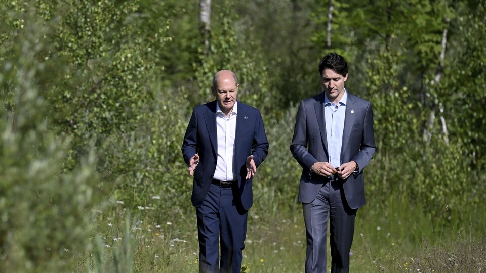 Olaf Scholz marche dans un champ à la droite de Justin Trudeau.