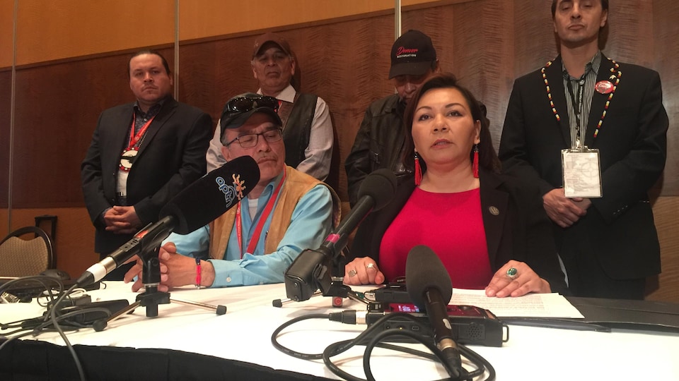 Une femme assise lors d'une conférence de presse avec quatre hommes derrière elle.