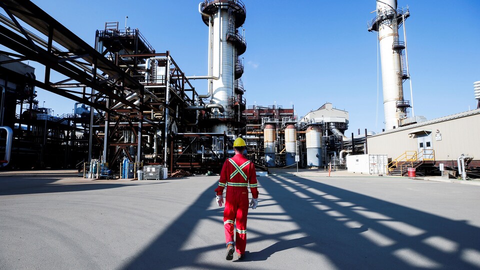 Un employé marche vers des installations industrielles.