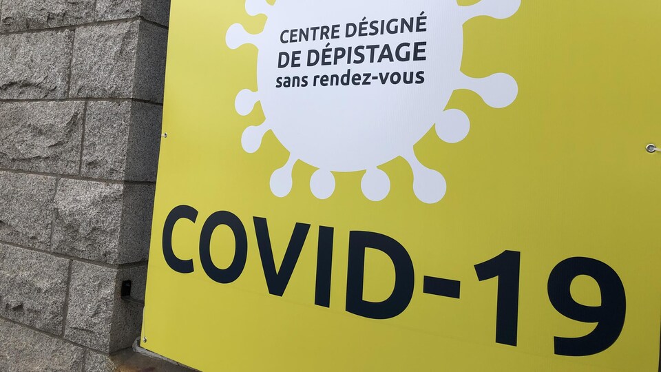Une affiche jaune indique où se trouve l'entrée d'un centre de dépistage de la COVID-19.