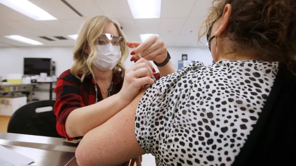 Une travailleuse administre le vaccin sur l'épaule d'une autre femme qui est de dos. 